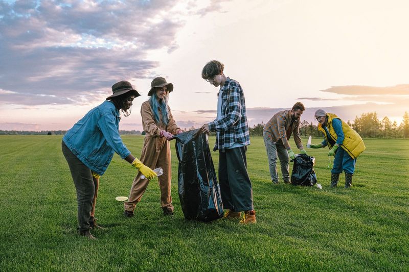 A group of volunteers picking up litter in a grassy field at sunset